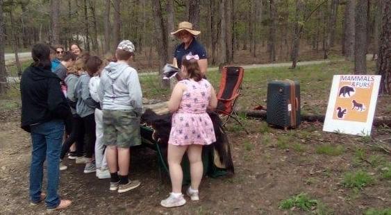 Students and presenter gathered around table with furs at the Mammal Furs station at the Eco Day at the Piney Wood Rec Area